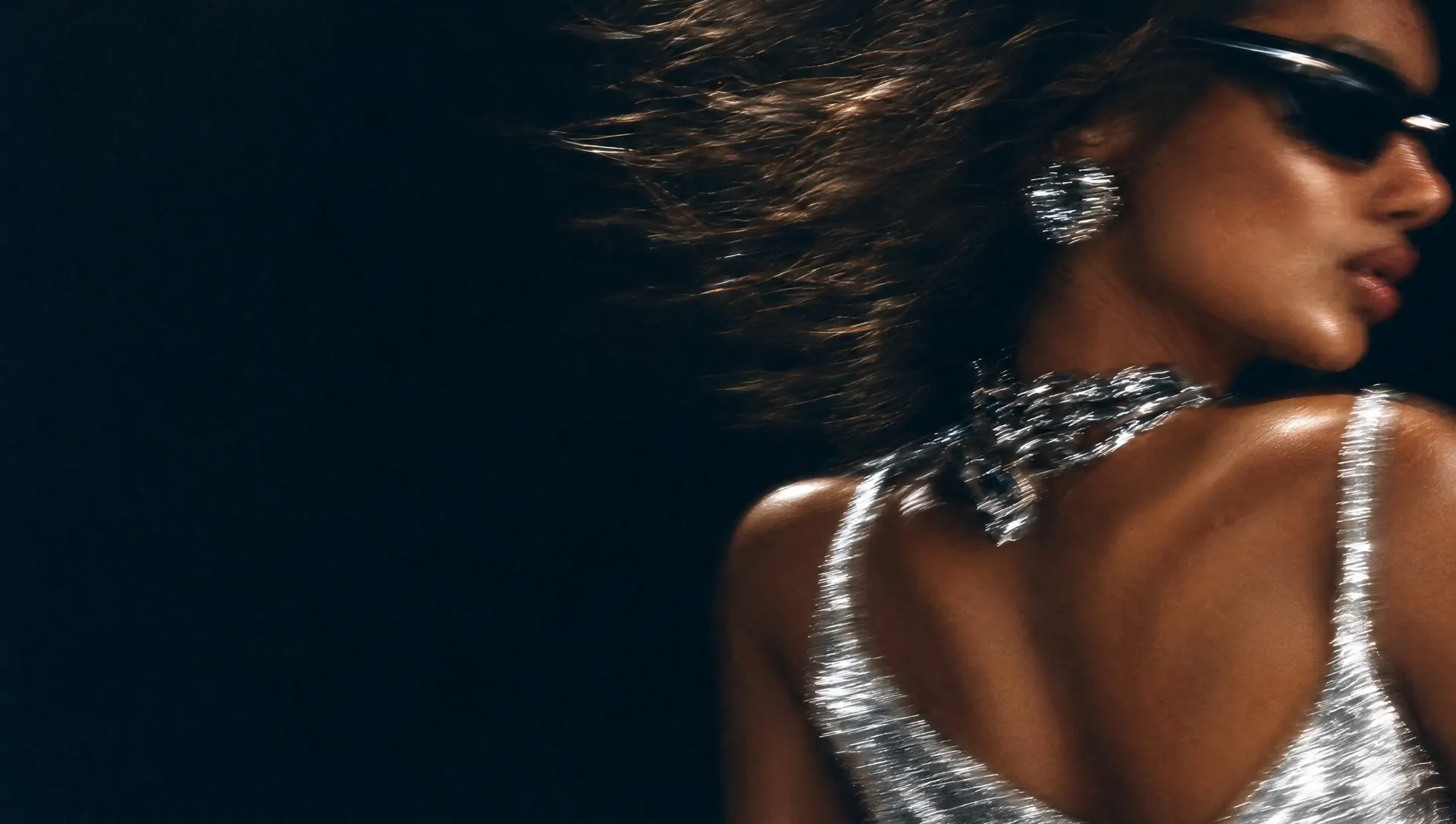The same woman turning away from the camera, hair flying, silver top and chain streaked by the flash.