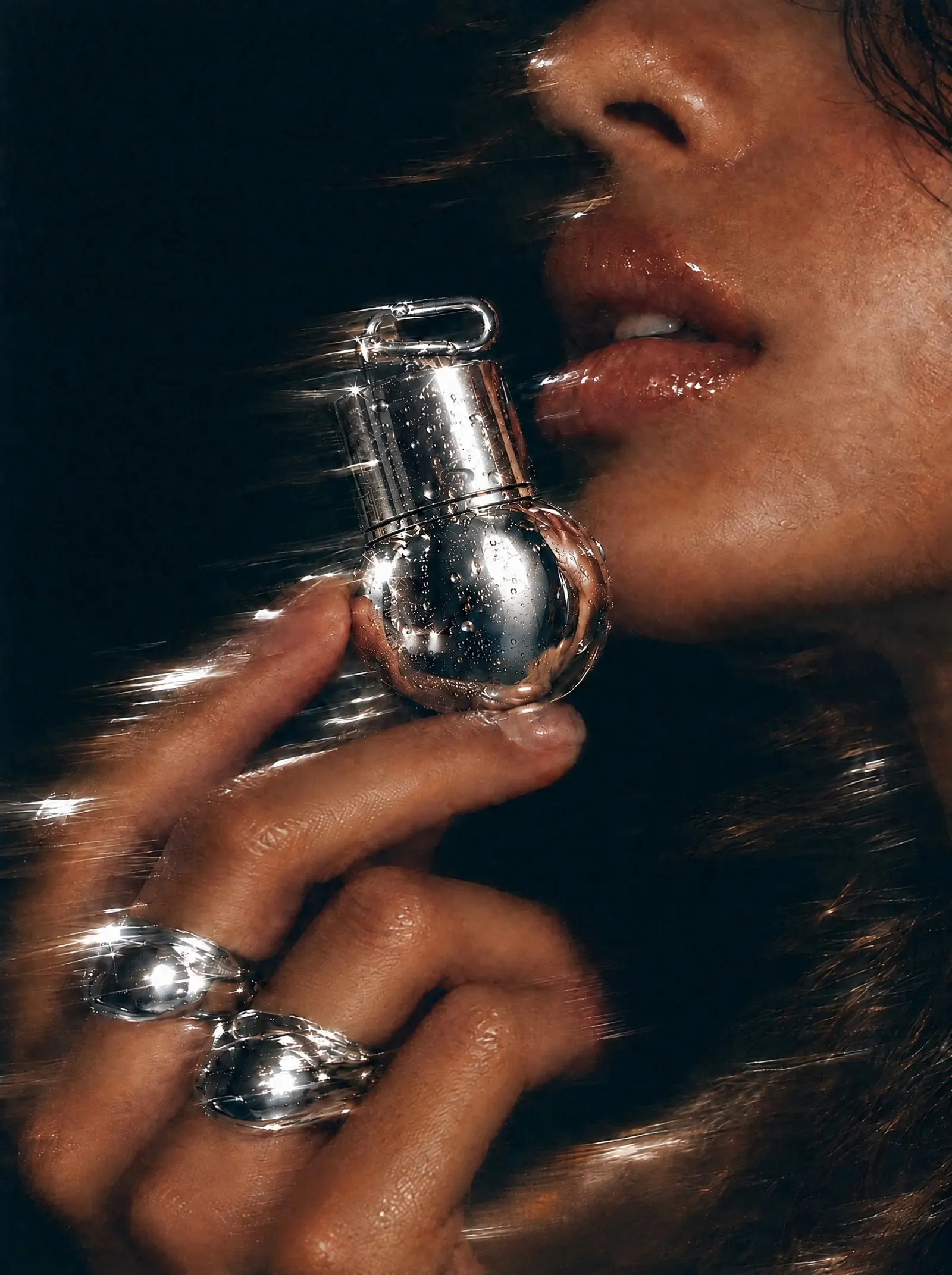 A woman in profile raises the chrome ORB, beaded with water, to her lips. Silver rings catch the flash.