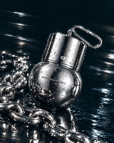 The chrome ORB lying on a wet black surface beside a heavy silver chain, covered in water droplets.
